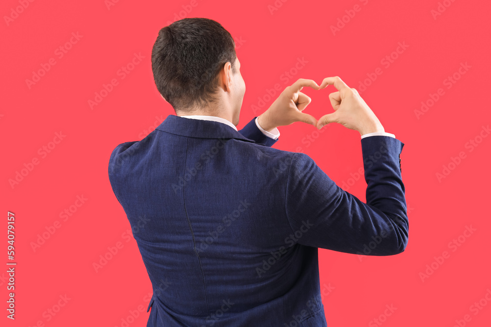 Young man making heart with his hands on red background, back view