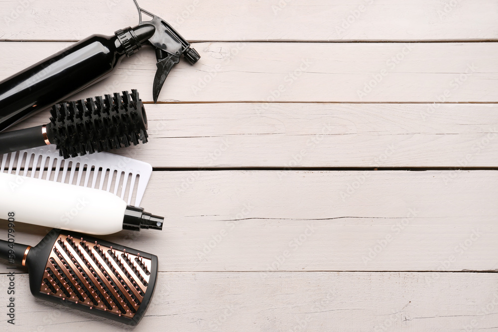 Hair brushes with spray bottles on light wooden background