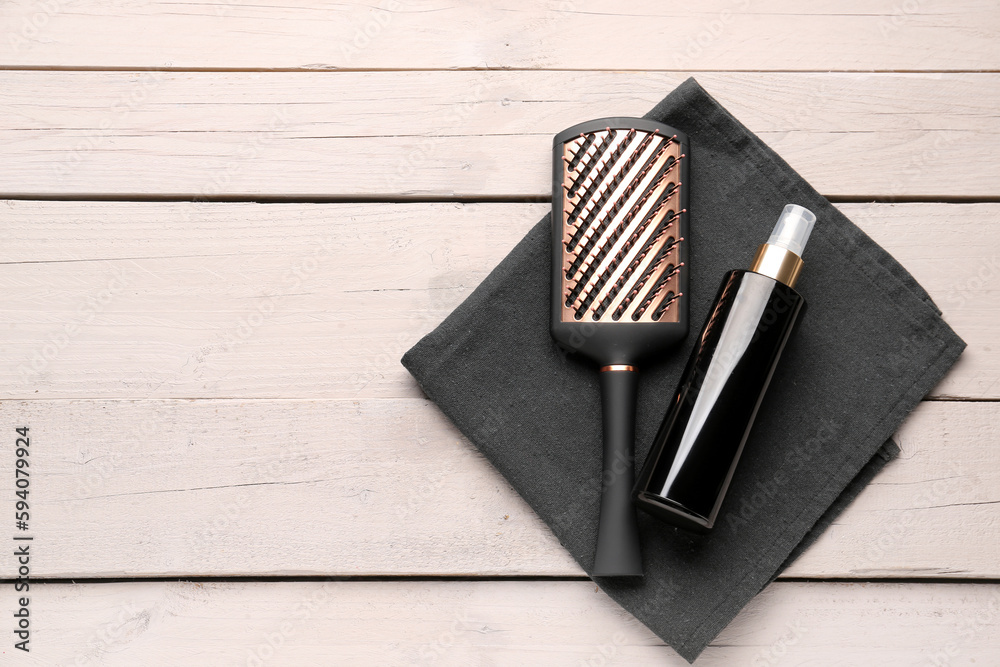 Hair brush with spray bottle and towel on light wooden background