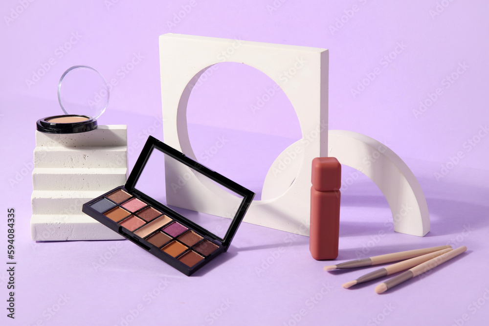 Eyeshadows with lipstick, brushes and podiums on lilac background