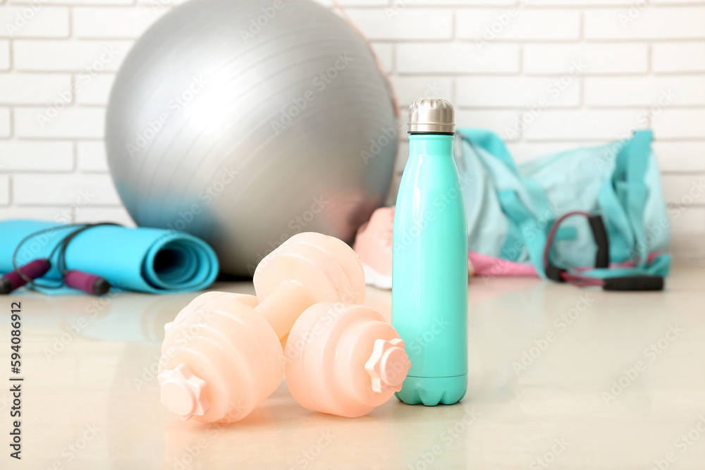 Dumbbells with sports water bottle in gym, closeup