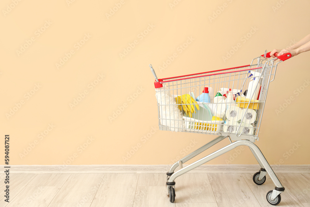 Shopping cart with cleaning supplies near beige wall