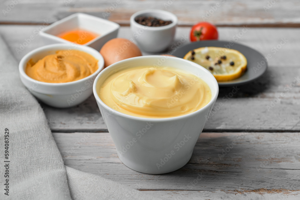 Bowl with tasty mayonnaise sauce and ingredients on light wooden background