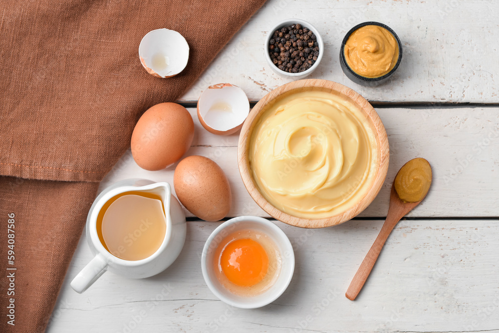 Bowl with tasty mayonnaise sauce and ingredients on light wooden background