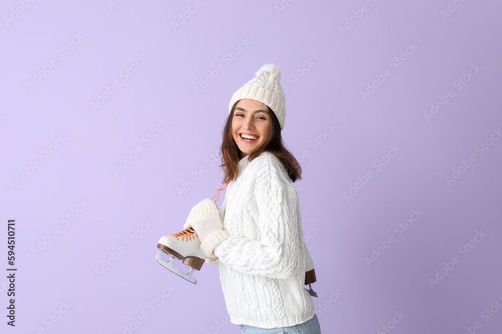 Pretty young woman with ice skates on lilac background