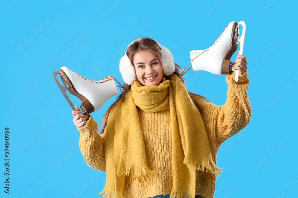 Pretty young woman with ice skates on blue background