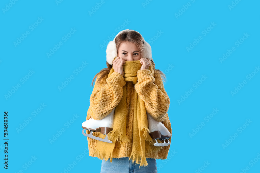 Pretty young woman with ice skates on blue background