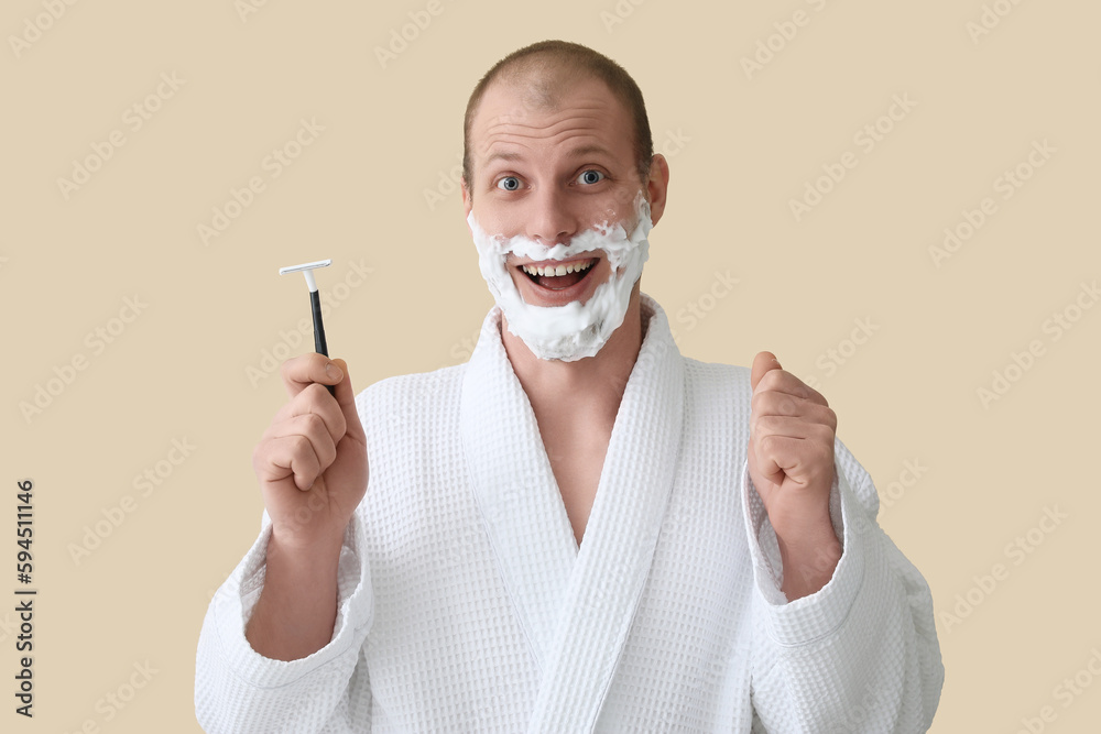 Happy young man shaving against beige background