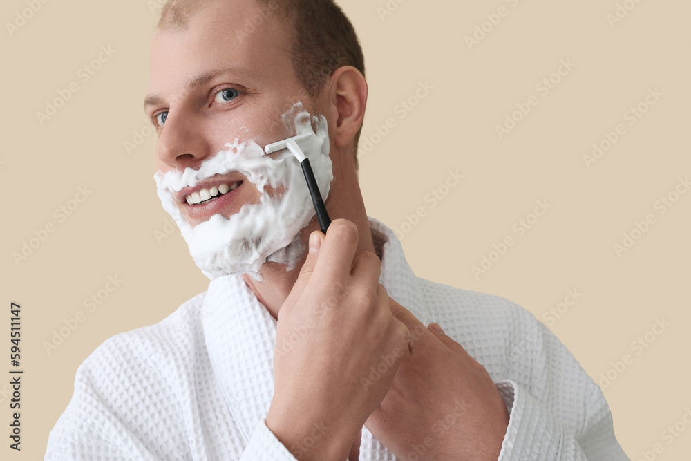 Young man shaving against beige background