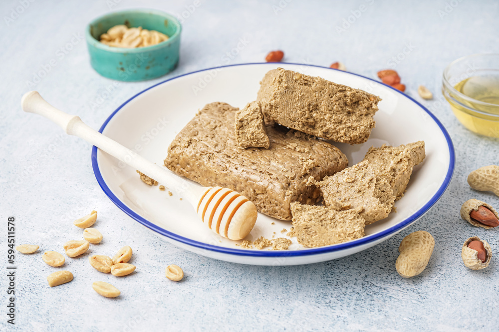 Plate of tasty halva and peanuts on light background