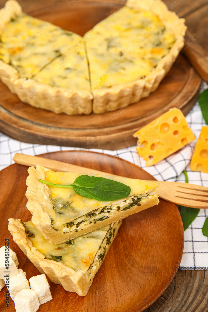 Plate and board with pieces of delicious quiche on brown wooden background