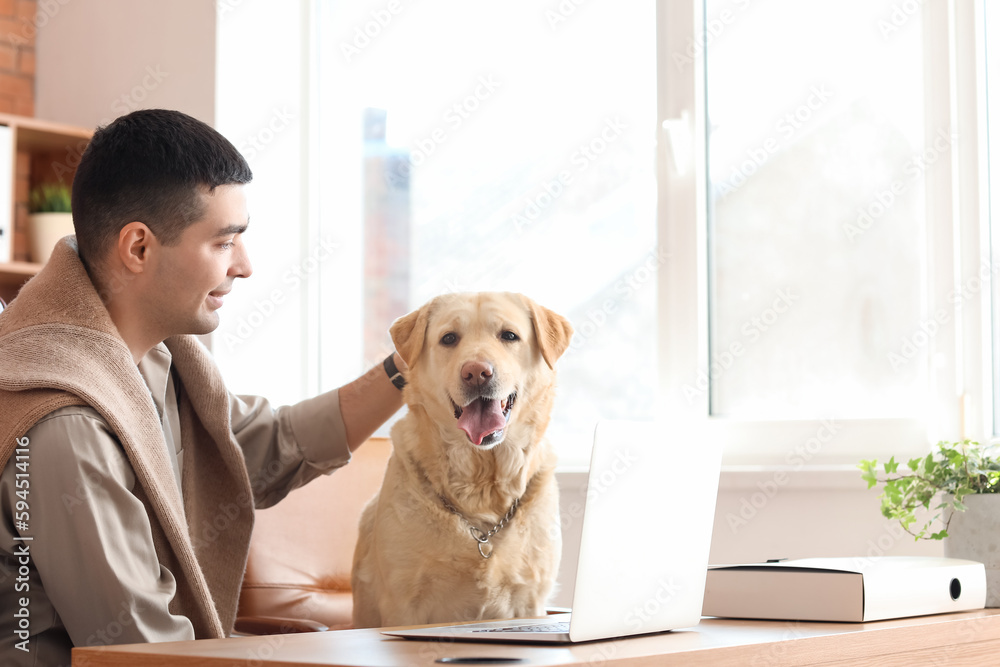 Young man with cute Labrador dog at table in office