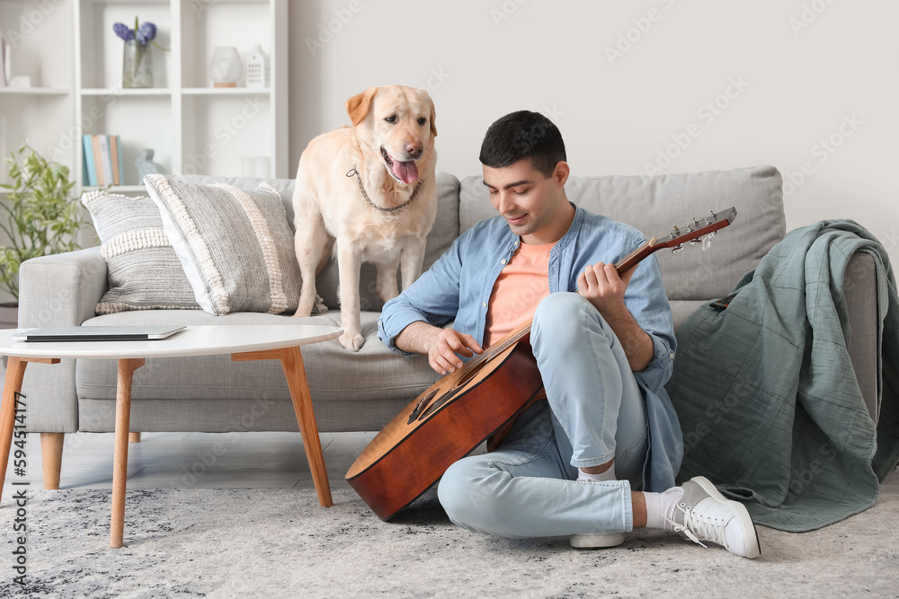 Young man with cute Labrador dog playing guitar at home