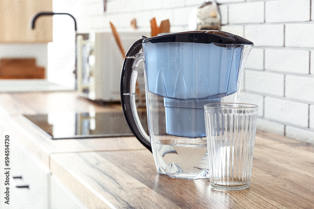 Modern filter jug and glass of water on kitchen counter