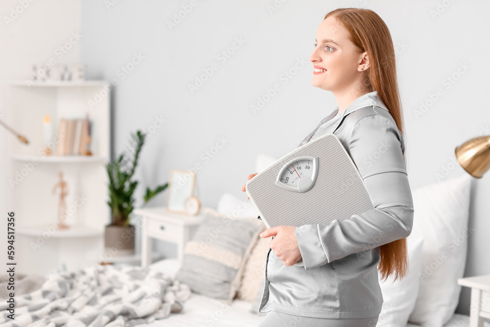 Young overweight woman with scales in bedroom