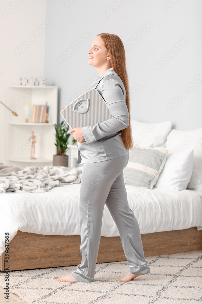 Young overweight woman with scales in bedroom