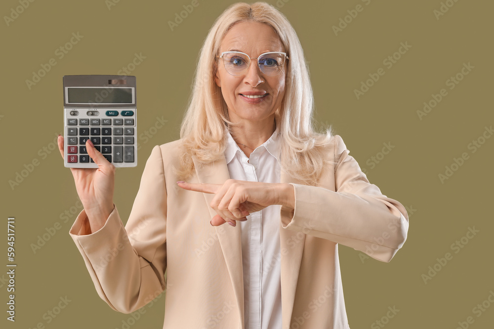 Mature woman pointing at calculator on green background