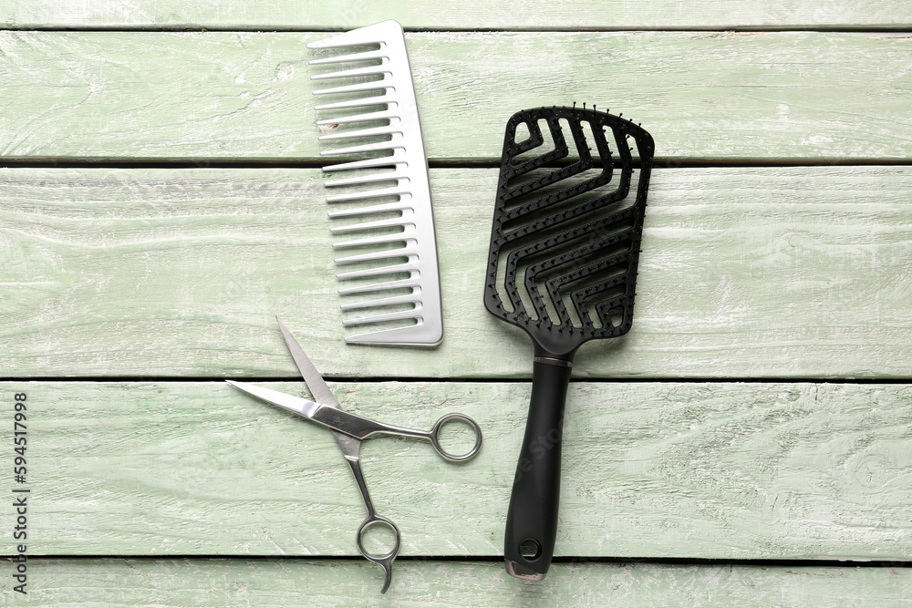 Hair brushes with scissors on green wooden background