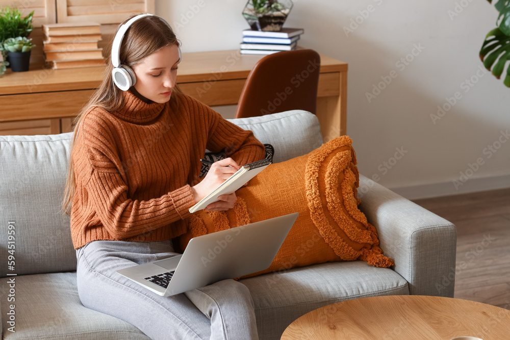 Female student with notebook studying online on sofa at home