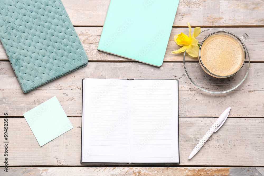 Composition with notebooks, sticky note, cup of coffee and narcissus flower on weathered wooden tabl