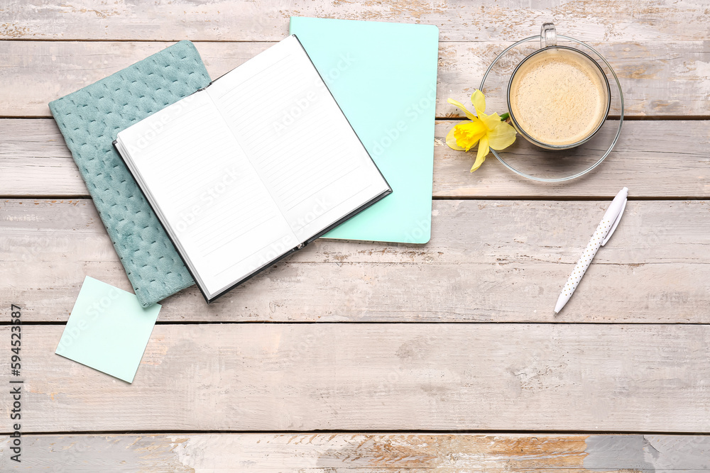 Composition with notebooks, sticky note, cup of coffee and narcissus flower on weathered wooden tabl