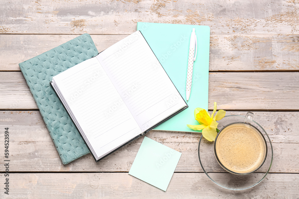 Composition with notebooks, sticky note, cup of coffee and narcissus flower on weathered wooden tabl