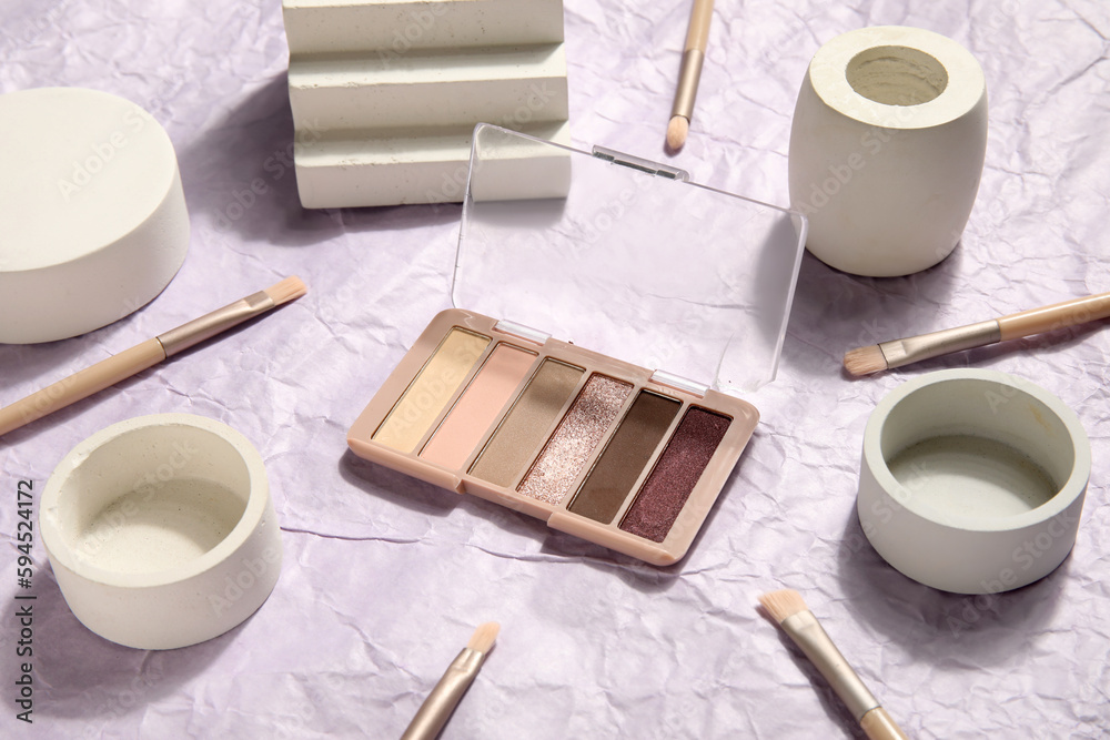 Eyeshadows with brushes and podiums on crumpled paper background