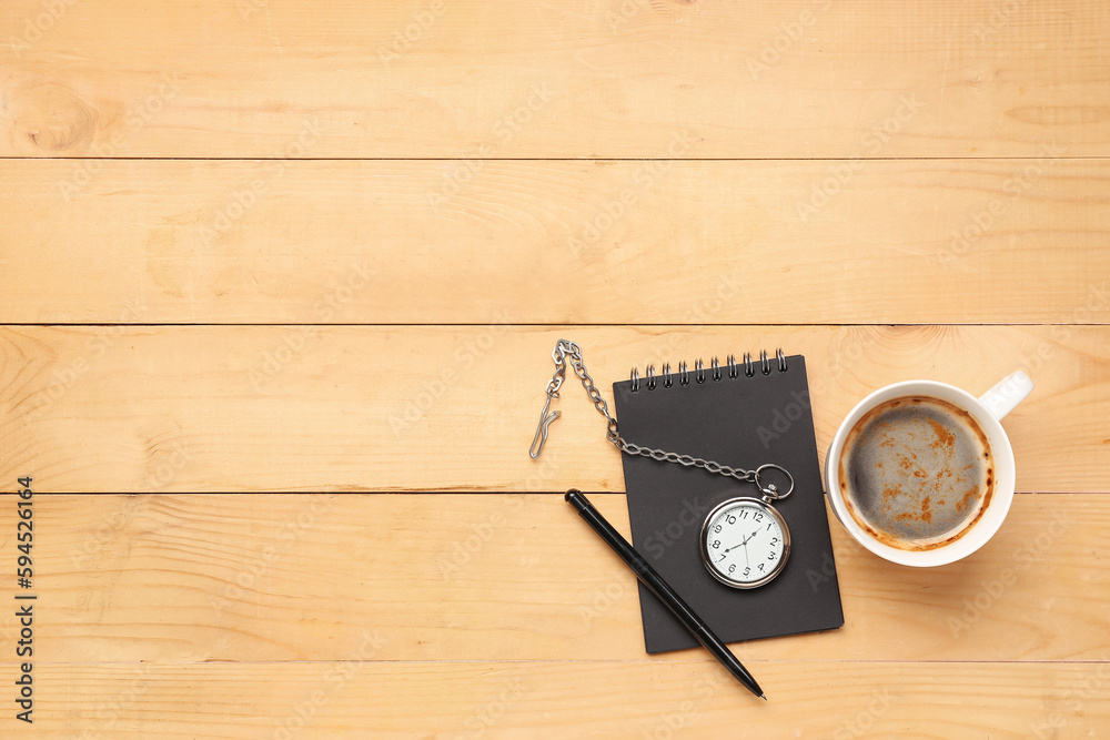 Cup of coffee with clock, pen and notebook on light wooden background