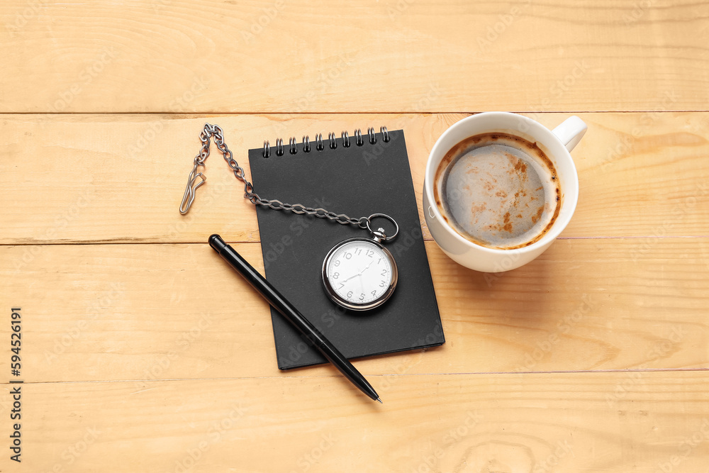 Cup of coffee with clock, pen and notebook on light wooden background