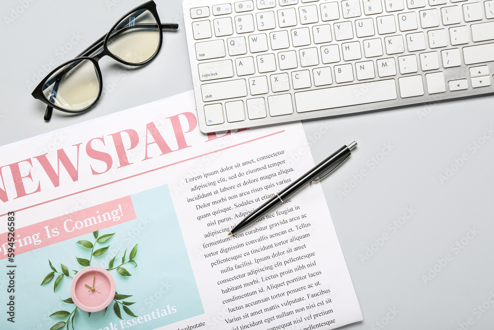 Newspaper with pen, computer keyboard and eyeglasses on light background, closeup