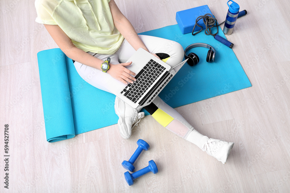 Sporty woman using laptop on mat in gym