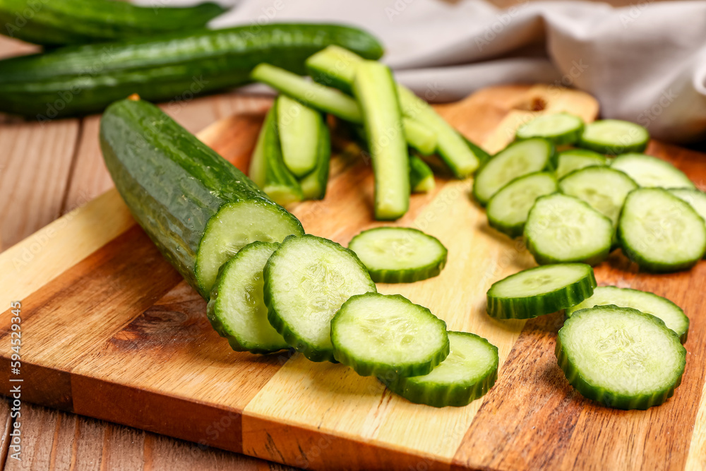 Board with fresh cut cucumber on wooden background, closeup