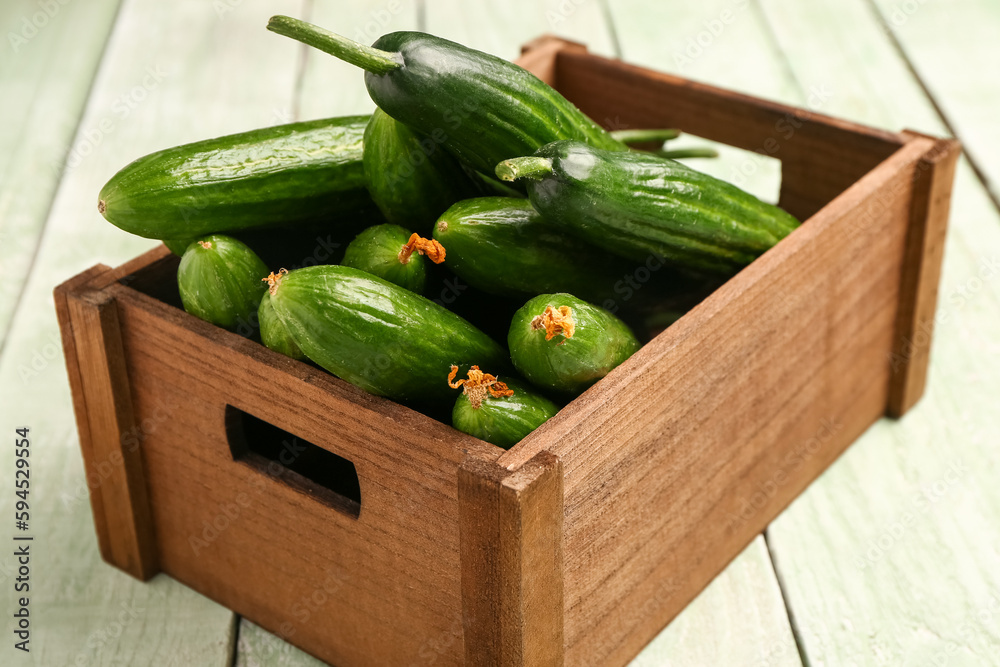 Box with fresh cucumbers on light wooden background