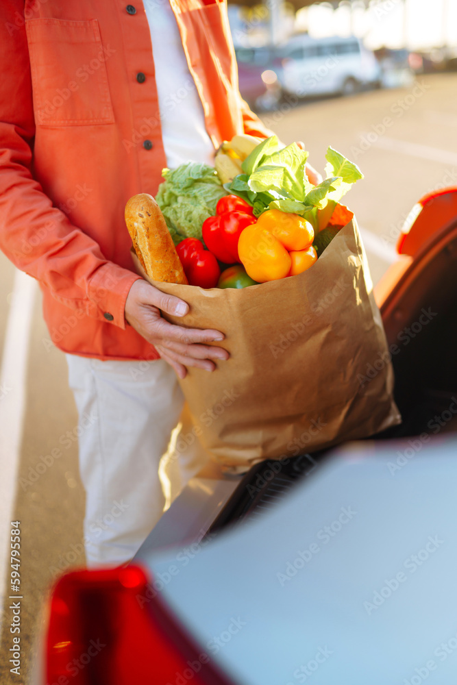  Stylish man with paper bags of vegetarian products in the parking lot near his car. Shopping for he