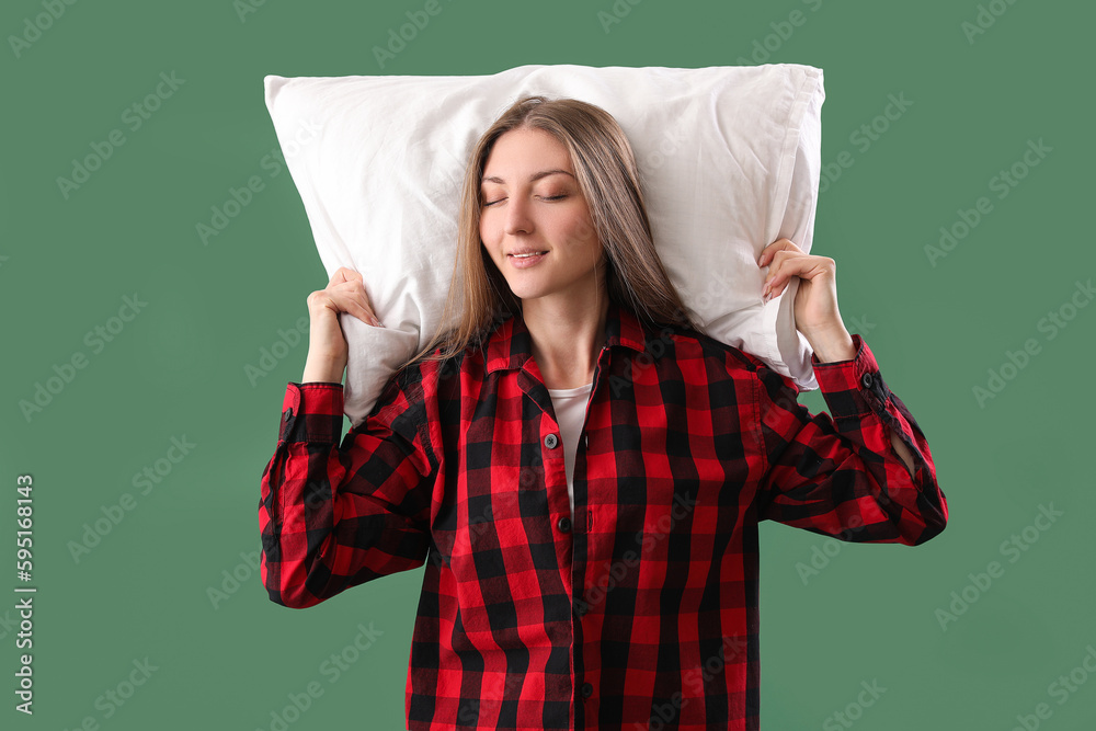 Young woman in pajamas with pillow on green background