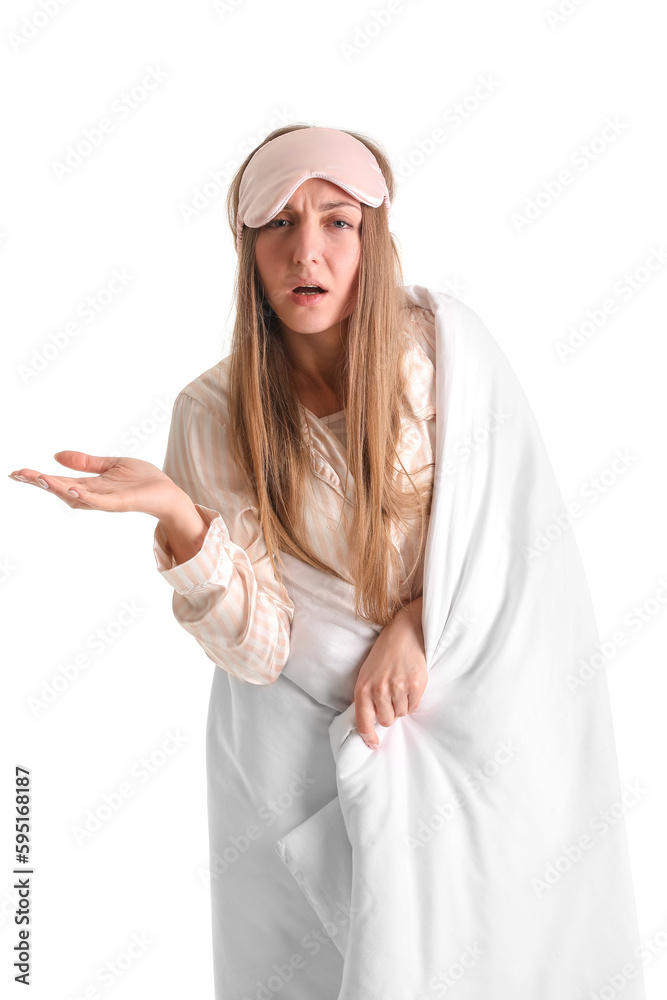 Upset young woman with sleeping mask and blanket on white background