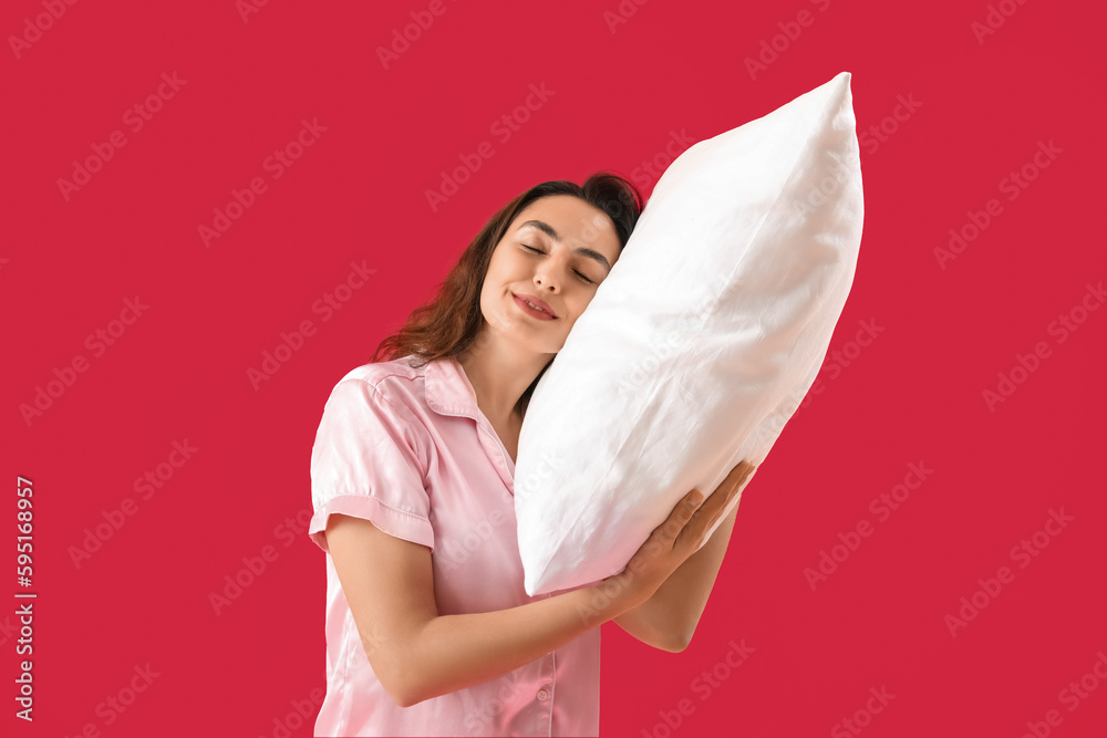 Young brunette woman in pajamas with pillow on pink background