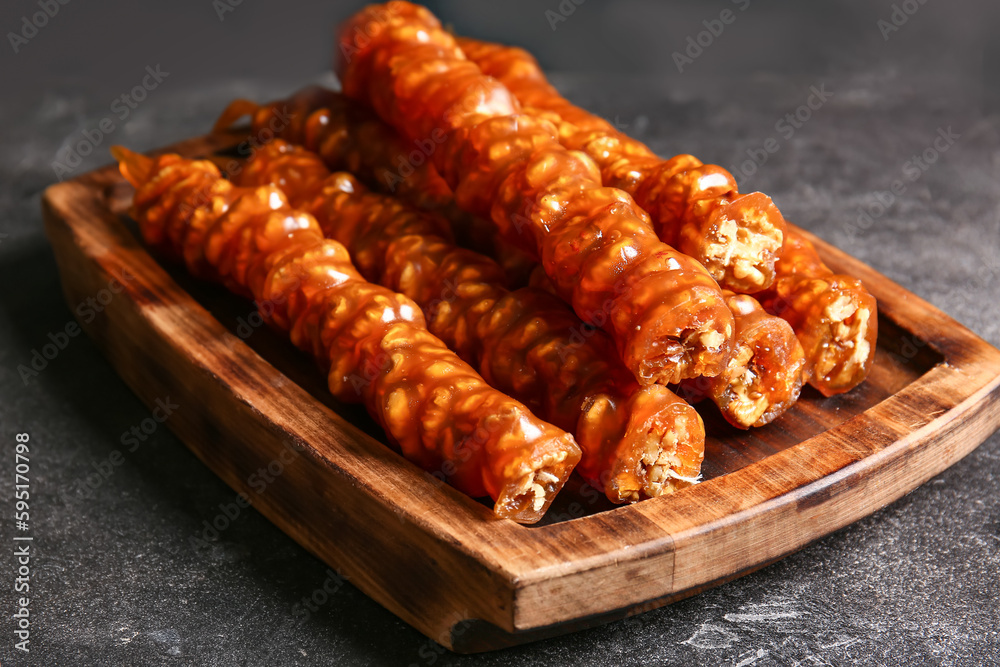 Wooden board with tasty churchkhela on dark background, closeup