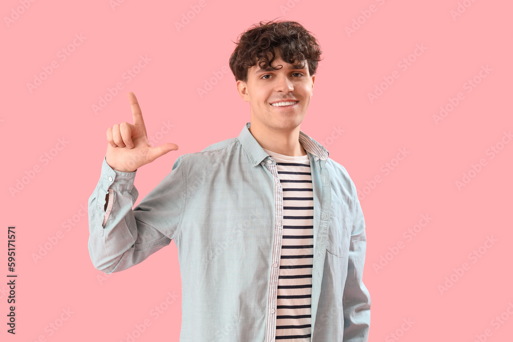 Young man showing loser gesture on pink background