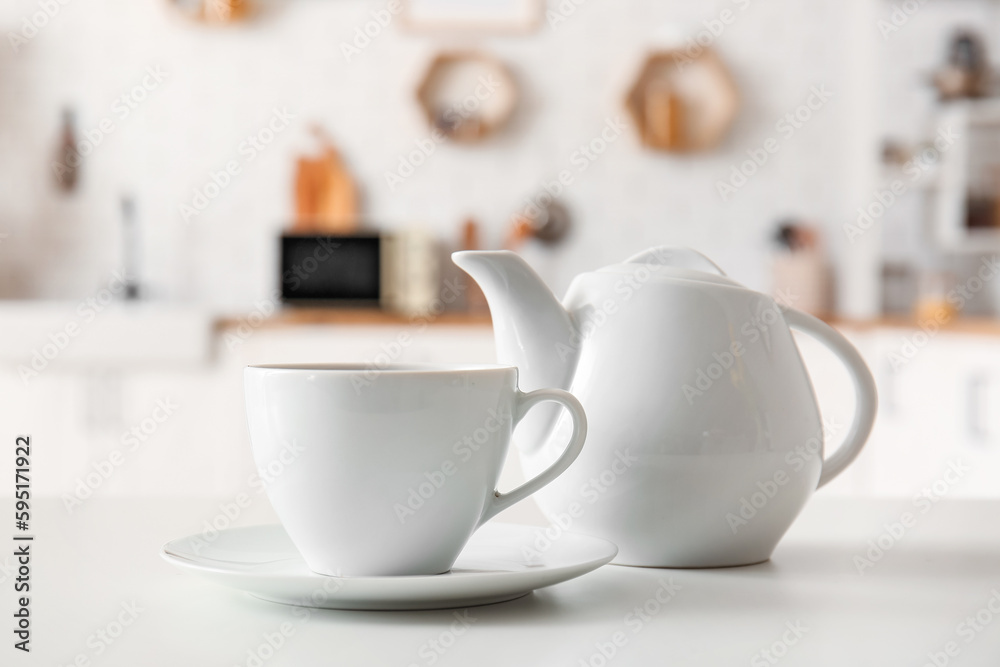 Cup and teapot on table in interior of modern kitchen, closeup