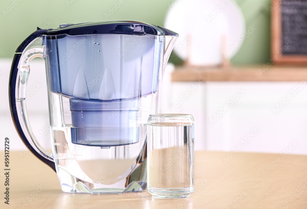 Modern filter jug and glass of water on wooden table in kitchen