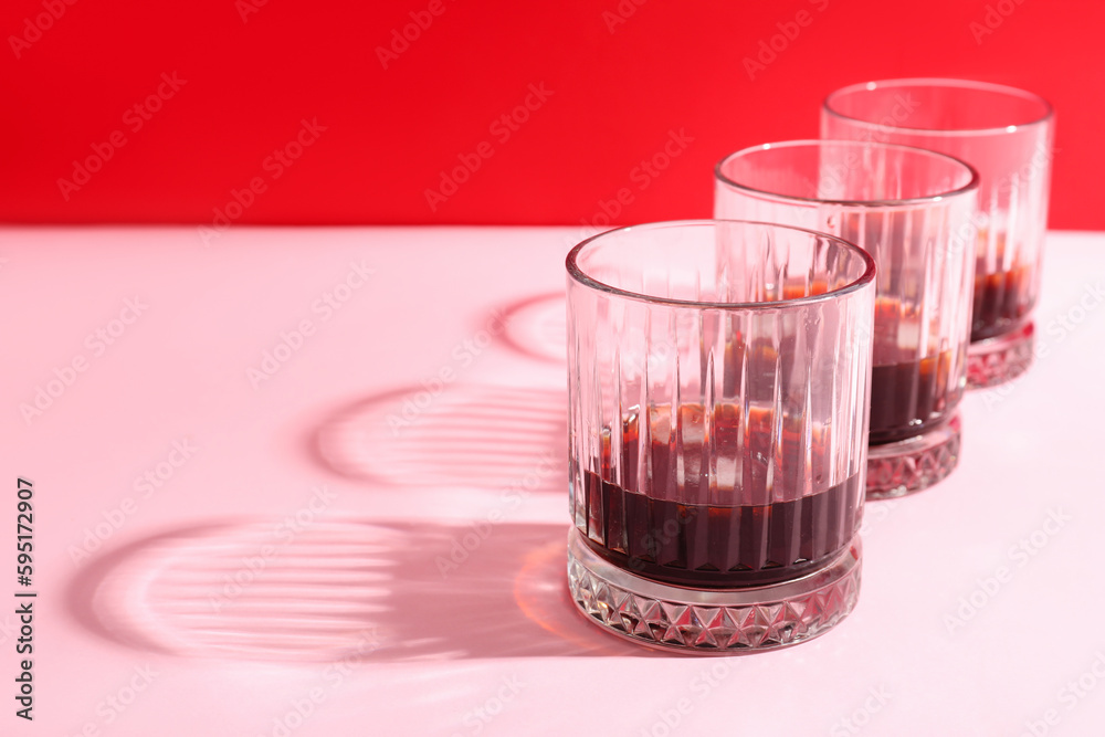 Glasses of rum with ice cubes on pink background