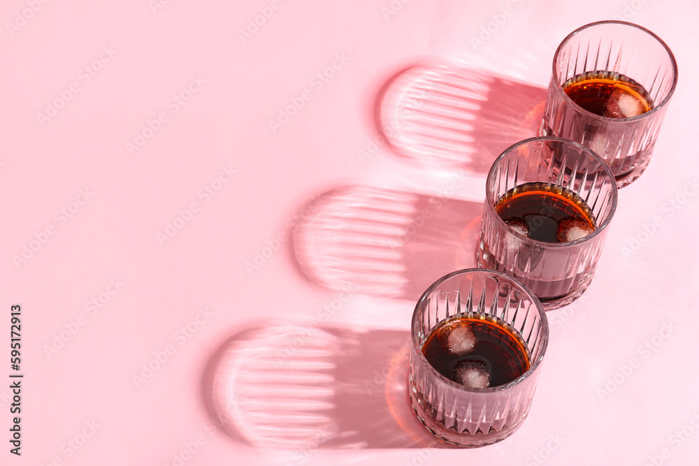 Glasses of rum with ice cubes on pink background