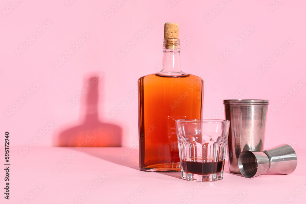 Bottle of rum, glass and measure cups on pink background