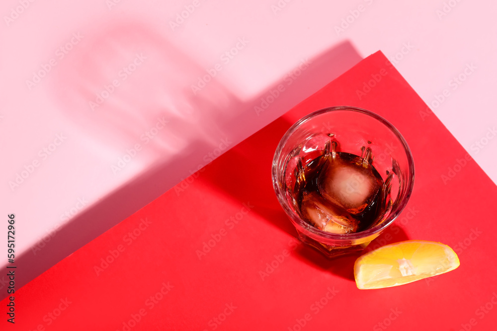 Glass of rum with ice cubes and lemon slice on colorful background