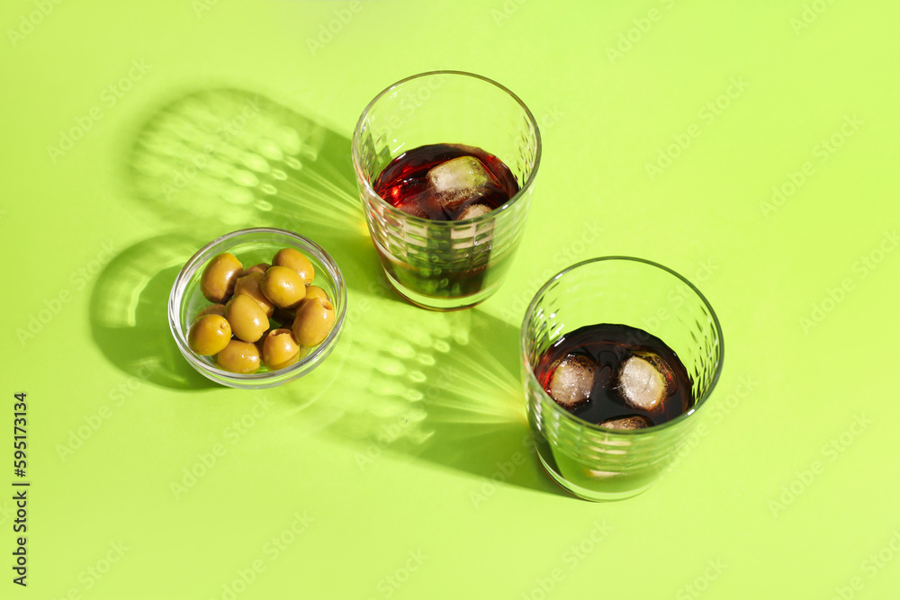 Glasses of rum with ice cubes and olives in bowl on green background