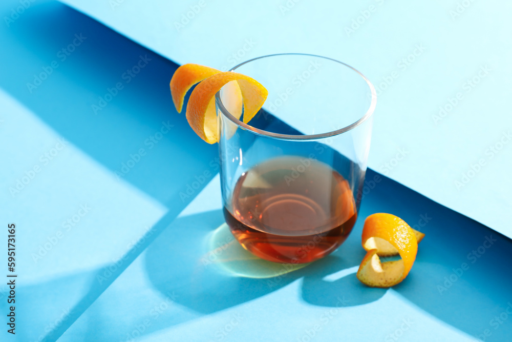 Glass of rum with orange peels on blue background