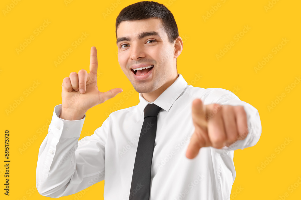 Young businessman showing loser gesture on yellow background, closeup