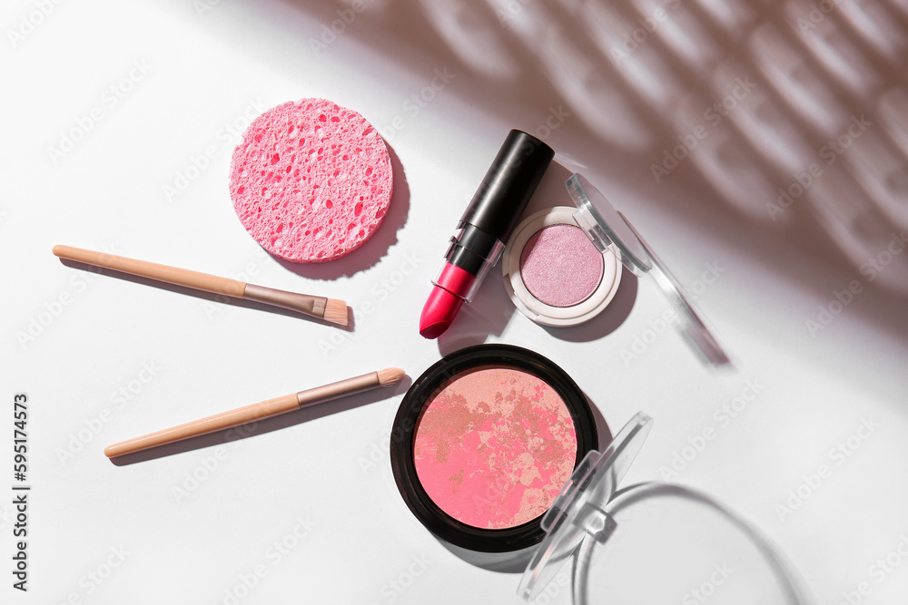 Lipstick, blush, eyeshadows, makeup brushes and sponge on light background