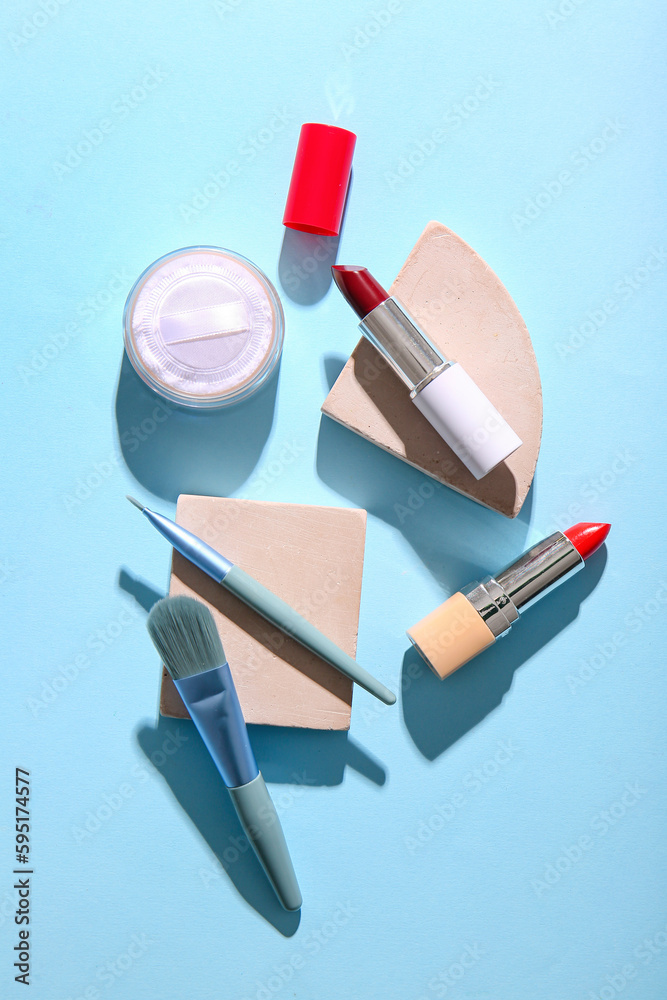 Plaster podiums with lipsticks, makeup powder and brushes on color background